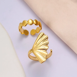 Macro detail of gold ginkgo leaf and seashell adjustable rings on white silk