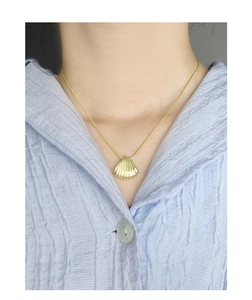 Golden shell pendant necklace close-up on model with elegant ribbed light blue shirt