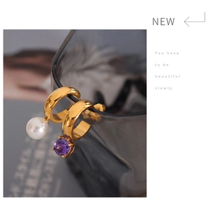 Detailed shot of asymmetric gold earrings with white pearl and purple zircon pendants