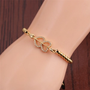 Macro view of gold heart arrow bracelet with white zircon inlay on wooden background