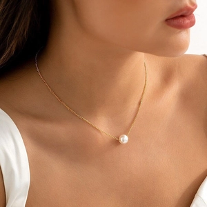 Close-up of elegant gold stainless steel necklace with a single white pearl on neck