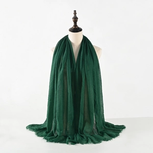 Detailed close-up of dark green crinkle cotton linen scarf with frayed tassel edges