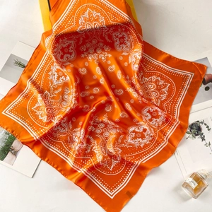 Close-up of bright orange paisley silk scarf with satin finish and floral detail texture