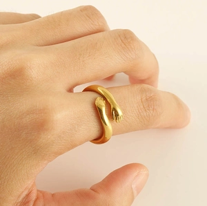 Detailed view of an 18k gold plated hug ring with two hands embracing on a finger