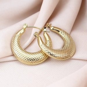 Detailed view of gold hoop earrings with textured scale pattern on pink silk