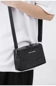Close-up of black crocodile pattern box bag with wide strap and metallic buckle