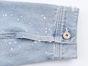 Détail de la veste en jean bleu clair avec des strass scintillants et un bouton en métal