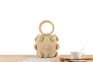 Detail of straw woven bucket bag with pearl flower accents on a rustic wooden table
