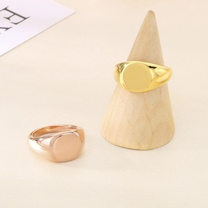 Polished 18K gold and rose gold signet rings on a minimalist wooden display stand