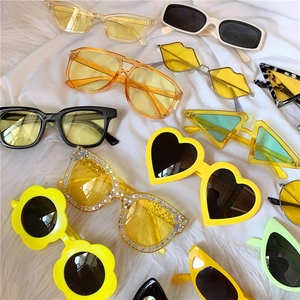 Flat lay of colorful daisy, heart, and star-shaped sunglasses on white fabric backdrop