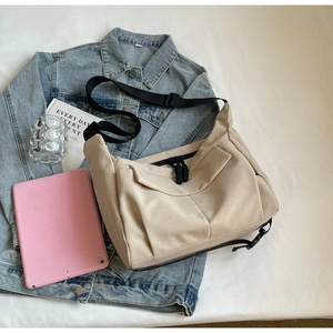 Detail of light beige canvas tote bag showing front zip pocket and black adjustable strap