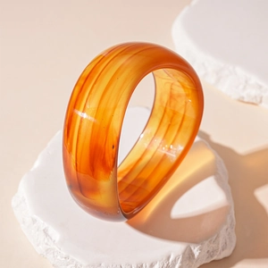 Macro view of wide geometric acrylic bangle with amber marble texture on white stone tray