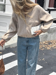 Detail of a beige zip-up casual jacket styled with light blue straight-leg denim jeans