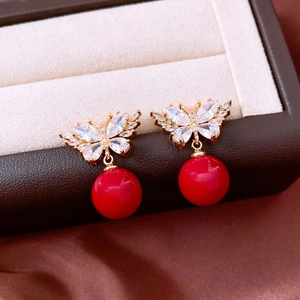 Detail of gold butterfly earrings with sparkling zircon and vibrant red round bead charms
