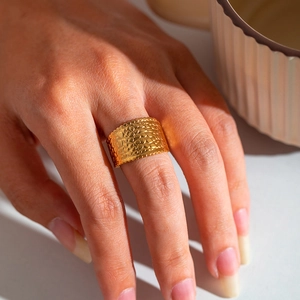 Detail of wide gold plated ring with hammered texture worn on finger for jewelry styling