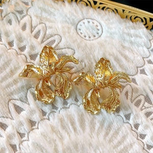 Detailed view of golden flower earrings with hammered metal texture on white plush
