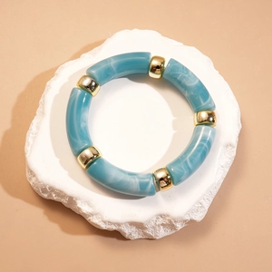 Détail du bracelet en résine marbrée bleue avec perles dorées sur socle blanc