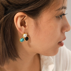Detail of gold earrings with pearl, turquoise and black stone on model's ear