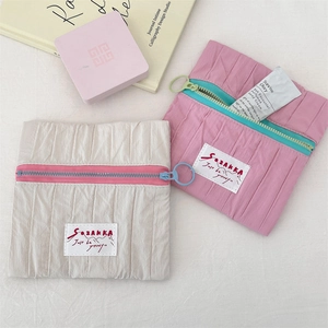 Detail view of small pleated fabric pouches with colorful ring zippers and woven labels