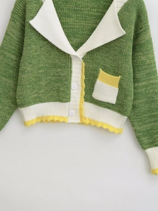 Detail of green knit cardigan with white V-neck collar, yellow wavy trim, and white buttons