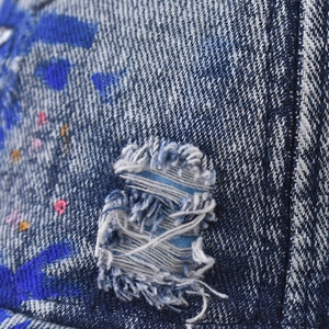 Close-up of washed denim fabric with distressed holes and colorful paint splatter details