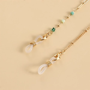 Close-up of golden metal eyeglass chain with green beads and adjustable silicone loops