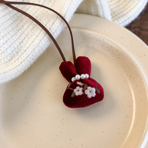 Detail of red velvet bunny necklace pouch with flower embroidery and pearl accents