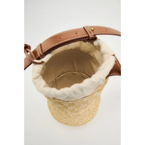 Handwoven straw bucket bag with brown leather straps and beige canvas drawstring closure