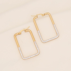 Macro shot of gold geometric earrings featuring sparkling white zircon stones on textured fabric