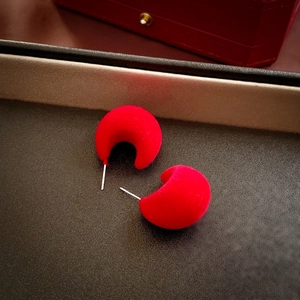Macro detail of red flocked C-shaped earrings with soft velvet texture and silver needles