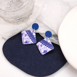 Close-up of blue and white porcelain pattern square earrings on dark blue velvet texture