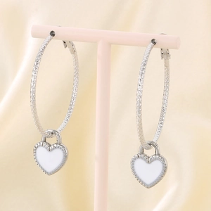 Detailed view of silver hoop earrings with white heart charms on silk fabric