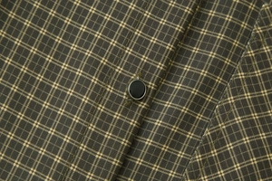Close-up of olive green checkered shirt fabric with a black metallic-edged button