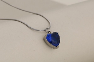 Macro shot of a blue heart-shaped crystal pendant on a silver snake chain necklace