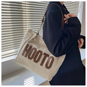Detail of canvas tote bag with HOOTO logo, leather trim, and metal chain shoulder strap