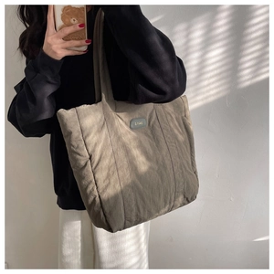 Model wearing a large green quilted nylon tote bag with natural sunlight and shadow