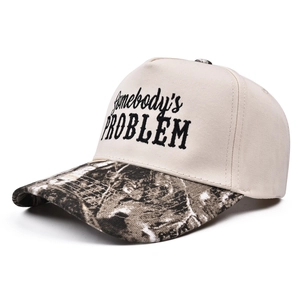 Detail of Somebody's Problem embroidery on beige trucker hat with camo brim