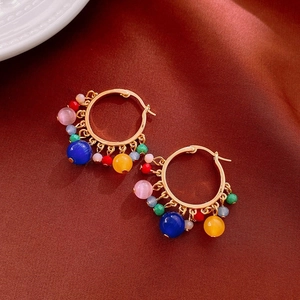 Détail de créoles bohèmes dorées avec perles multicolores sur fond de soie luxueuse