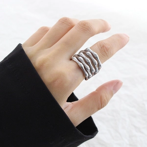Detail view of a silver hollow skeleton ring worn on fingers over white fabric