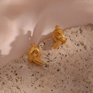 Detail of golden knot stud earrings on rocky texture with soft silk background