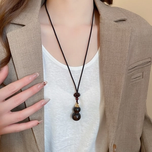 Detail view of a handcrafted wood gourd pendant necklace on a model wearing a blazer