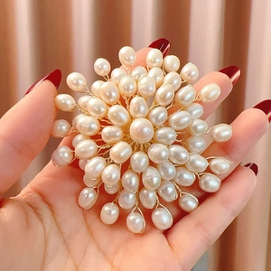 Detailed view of a handmade freshwater pearl flower brooch held by hand for scale