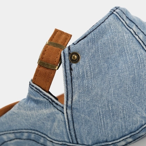 Detail of denim beret featuring blue washed fabric, brown leather strap and bronze buckle