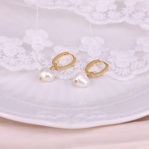Detailed shot of golden pearl earrings with zircon inlay on a vintage porcelain plate