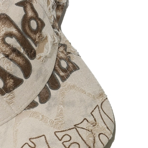 Close-up of distressed beige canvas baseball cap with gothic lettering and worn details