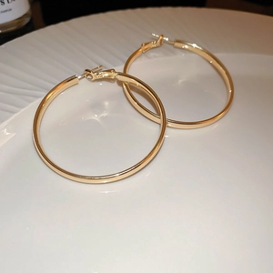 Detailed view of glossy gold geometric hoop earrings on a white ceramic tray
