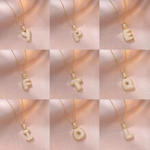 Detailed grid of golden initial pendants with cream textured finish on pink silk fabric