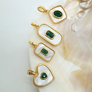 Macro detail of 18k gold plated shell pendants with emerald green gemstones