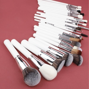 Macro view of 30-piece makeup brush set with white handles and silver ferrules on red surface
