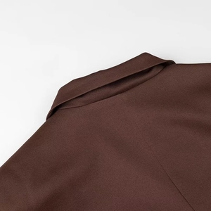 Détail d'un blazer marron foncé montrant le revers asymétrique et la texture du tissu